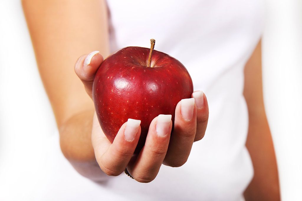 Mujer haciendo una buena elección de alimentos saludables agarrando una manzana roja con la mano